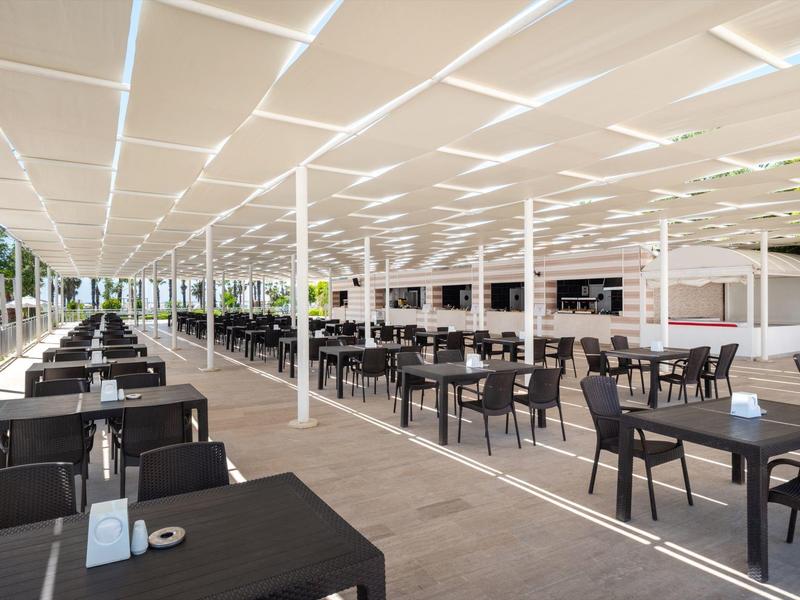 Groot modern buitenterras van een restaurant met zwarte tafels en stoelen onder een wit zonnescherm.