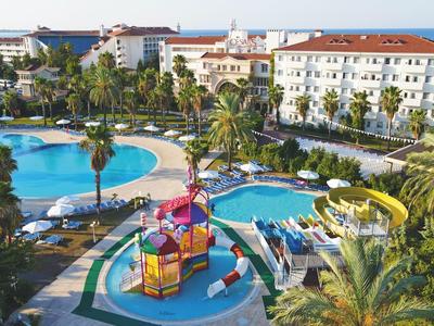 Resort con piscine, scivolo, area giochi e lettini circondati da palme.
