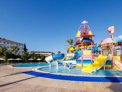Area giochi acquatica colorata con scivoli accanto a una grande piscina sotto un cielo sereno.