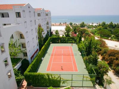 Pista de tenis junto a un edificio blanco del hotel con vista al mar y jardines.