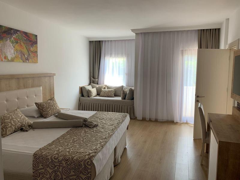 Camera d'hotel accogliente con letti matrimoniali, seduta alla finestra, tende morbide e illuminazione calda.