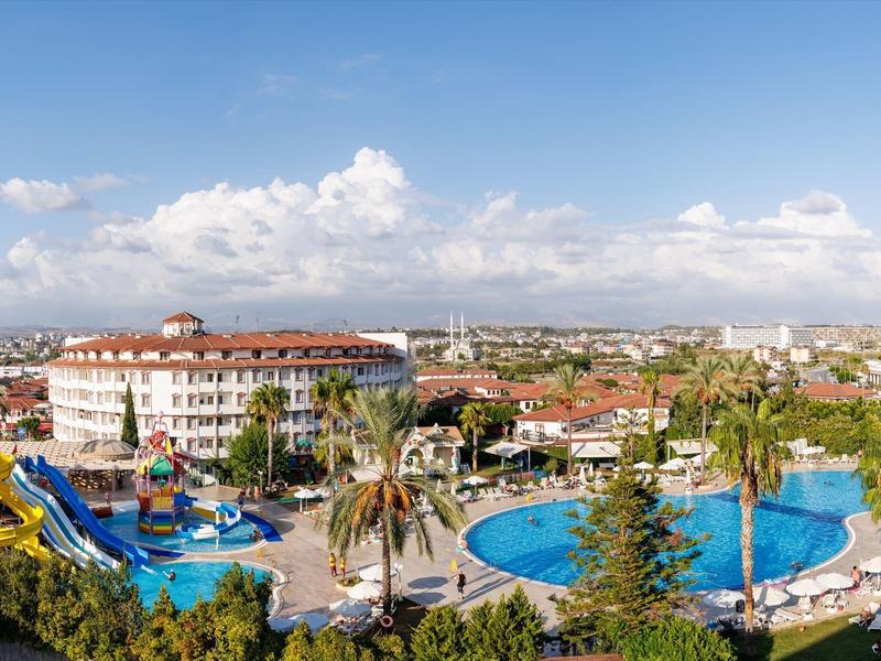 Hotel con grande piscina, scivoli d'acqua, circondato da palme sotto un cielo parzialmente nuvoloso.