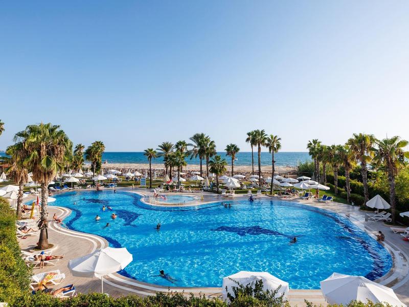 Piscina del resort con palme e vista sull'oceano sotto un cielo azzurro sereno.