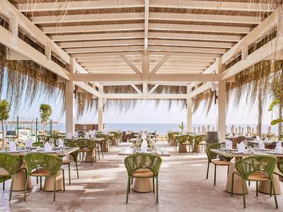 Ristorante all'aperto con tetto in legno con vista sul mare, sedie verdi e tavoli elegantemente apparecchiati.