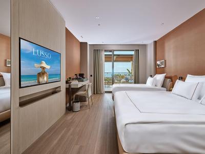 Habitación de hotel moderna con cama doble, escritorio, TV y balcón con vista al mar.