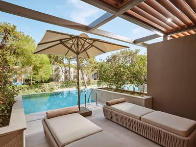 Terrazza con due lettini e ombrellone accanto a una piscina con vista sugli alberi.