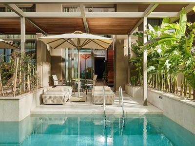 Piscina esterna moderna con area salotto e ombrellone accanto alla camera d'hotel
