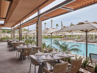 Terrassenrestaurant mit gedeckten Tischen neben großem Pool und Sonnenschirmen, helle Holzdachkonstruktion.