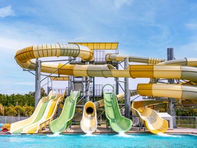 Più scivoli d'acqua colorati sfociano in una piscina sotto un cielo blu.