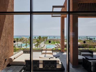 Vista attraverso finestre di vetro su terrazza con divani e piscina, mare sullo sfondo.