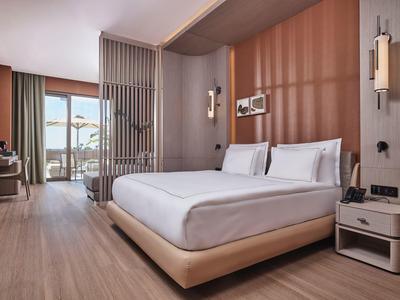 Camera d'albergo moderna con letto grande, pavimento in legno e balcone con vista sul mare.