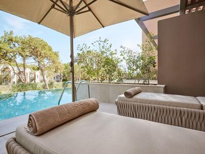 Lettini con asciugamani sotto ombrellone vicino a piscina e alberi.