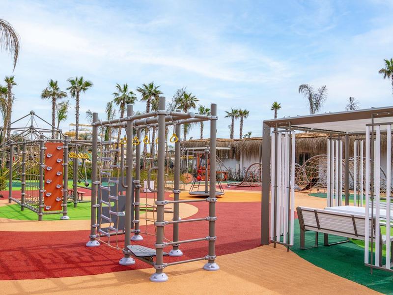 Area esterna moderna con strutture per arrampicata e palme sotto un cielo blu.