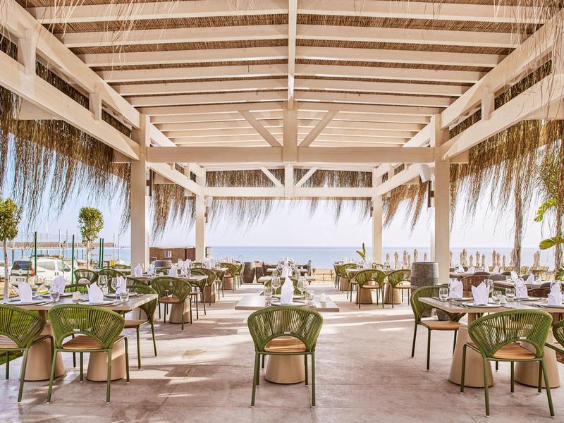 Ristorante all'aperto con tetto in legno con vista sul mare, sedie verdi e tavoli elegantemente apparecchiati.
