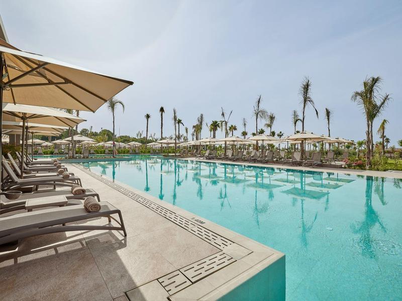 Vista di una grande piscina con lettini e ombrelloni in un resort tropicale.