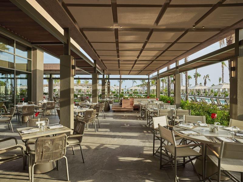 Area esterna moderna del ristorante con tavoli apparecchiati e vista sulle palme.