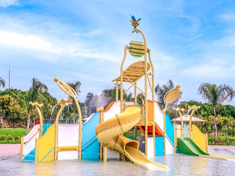 Area giochi acquatica colorata con scivoli e ombrelloni sotto un cielo sereno.