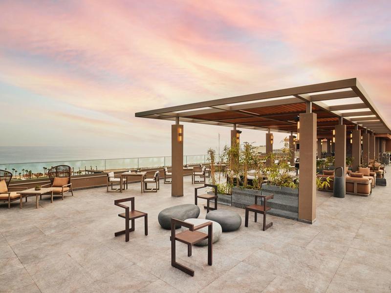 Terrazza sul tetto con zona salotto e pergola al tramonto con vista sul mare.