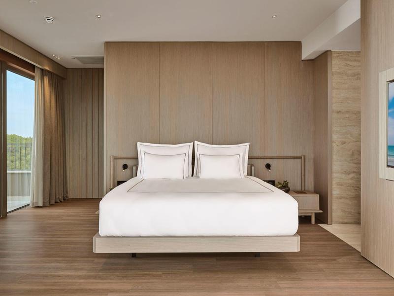 Camera d'hotel moderna con letto grande, pavimento in legno e grande finestra con vista sulla natura.