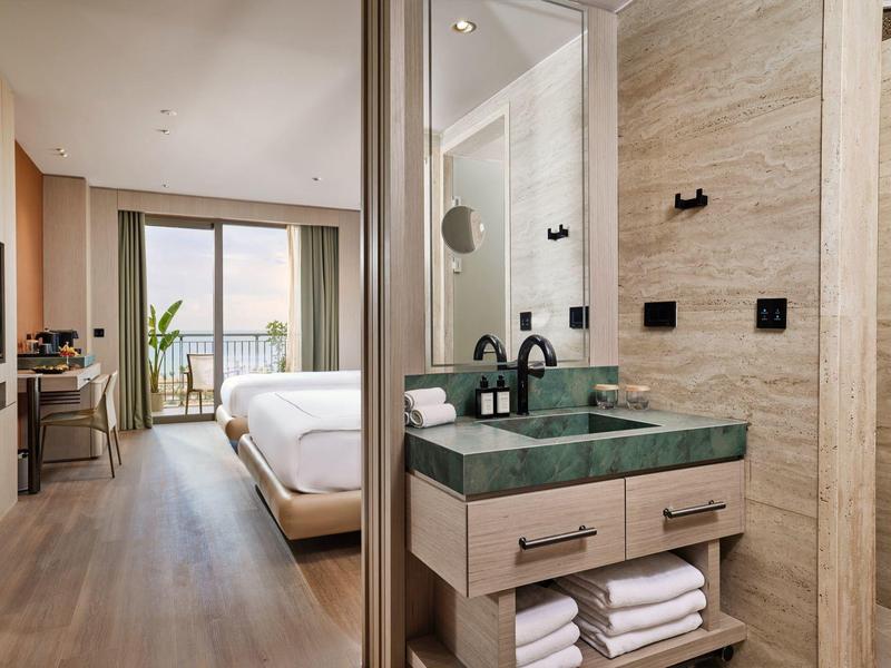 Camera d'hotel moderna con bagno, pavimento in legno e balcone con vista mare.