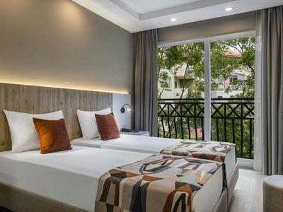 Modern eingerichtetes Hotelzimmer mit zwei Einzelbetten und Blick auf einen Balkon mit Bäumen.