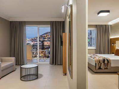 Modern eingerichtetes Hotelzimmer mit Balkon und Blick auf eine Stadt bei Dämmerung.