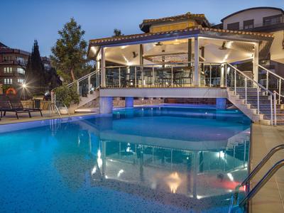 Beleuchteter Poolbereich eines Hotels mit moderner Terrasse und Sitzgelegenheiten bei Nacht.