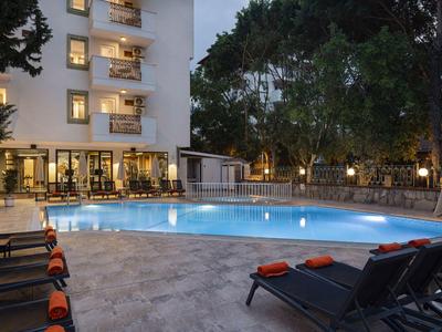 Beleuchteter Hotelpool bei Nacht mit Liegestühlen und Bäumen im Hintergrund.