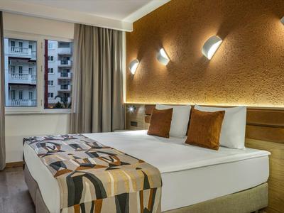 Modernes Hotelzimmer mit Doppelbett, warmem Licht und Blick auf städtische Gebäude.