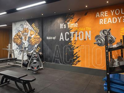 Fitnessraum mit Gewichten, Bank und motivierender Wandgestaltung in Orange und Schwarz.