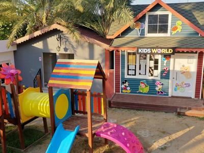 Aire de jeux colorée pour enfants avec toboggans et tunnel devant un bâtiment nommé 'Kids World'.