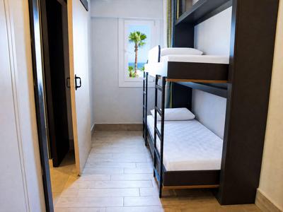 Smalle hotelkamerhoek met stapelbed en raam met uitzicht op palmbomen.