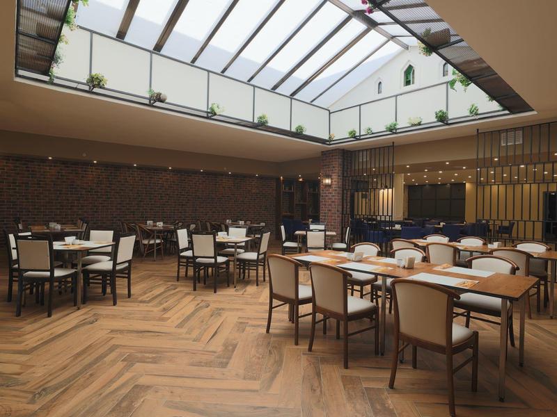 Světla moderní restaurace se skleněnou střechou a dřevěnými podlahami, vybavená stoly a židlemi.