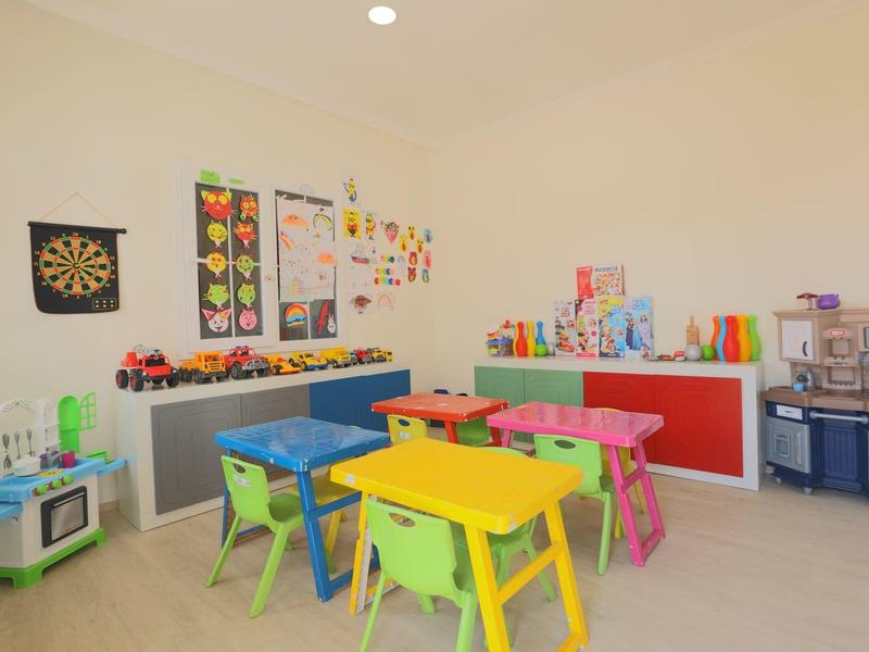 Světlou dětskou hernu s barevnými stoly, židlemi a hračkami v místnosti.