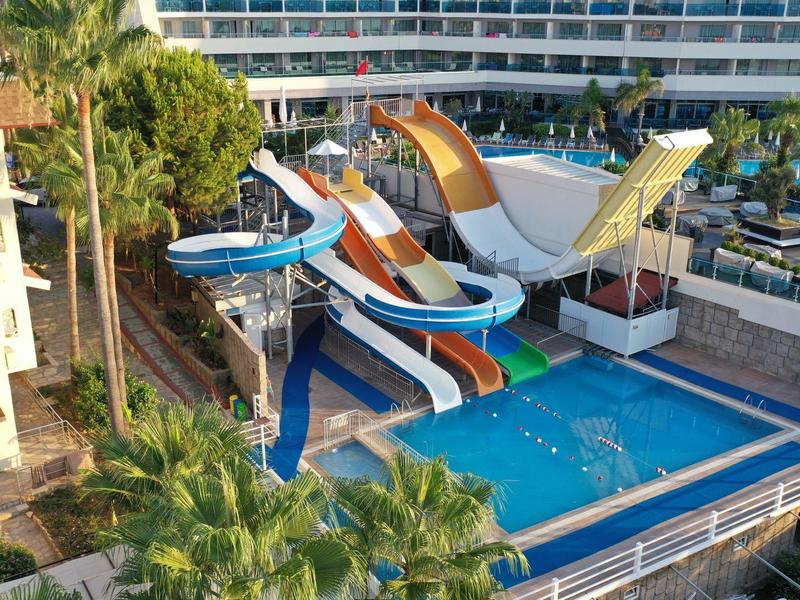 Barevné vodní skluzavky v hotelové bazénové oblasti obklopené palmovými stromy.