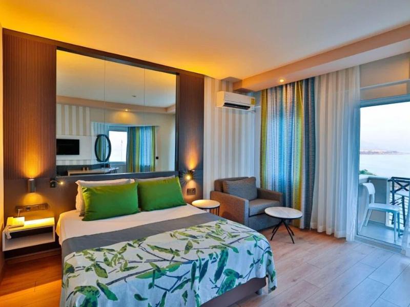 Moderně zařízený hotelový pokoj s manželskou postelí, balkónem a denním světlem z velkých oken.