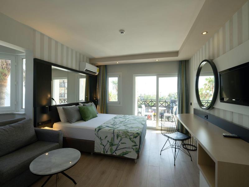 Moderní hotelový pokoj s manželskou postelí, balkónem a posezením.