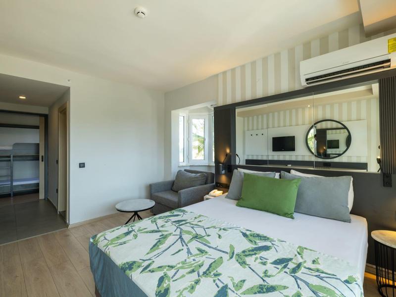 Moderně zařízený hotelový pokoj s manželskou postelí, klimatizací a koupelnou v pozadí.