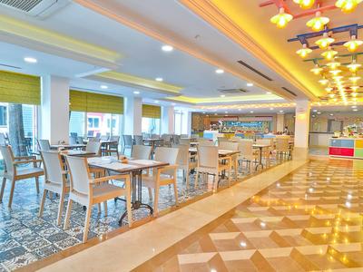 Světlá hotelová jídelna s moderními židlemi, stoly a žlutými akcenty.