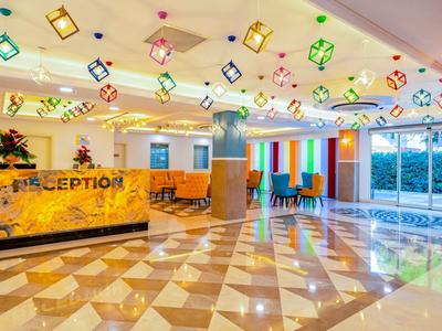 Světlá hotelová lobby s recepcí, barevnými závěsnými lampami a dostatkem denního světla z velkých oken.