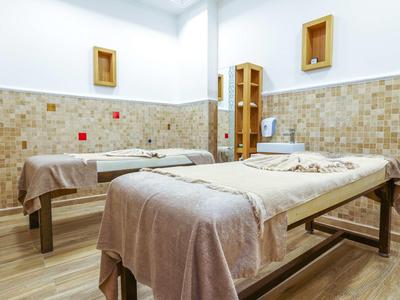 Dvě masážní lehátka v jasné místnosti s béžovými dlaždicemi a dřevěnými rámy na stěně.