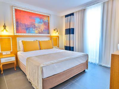 Modern ingerichte hotelkamer met tweepersoonsbed, warme gele tinten en groot raam met gordijnen.