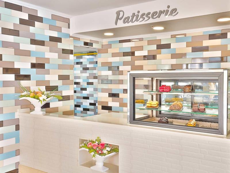 Moderní cukrárna s barevným mozaikovým vzorem dlaždic a vitrínou plnou pečiva.