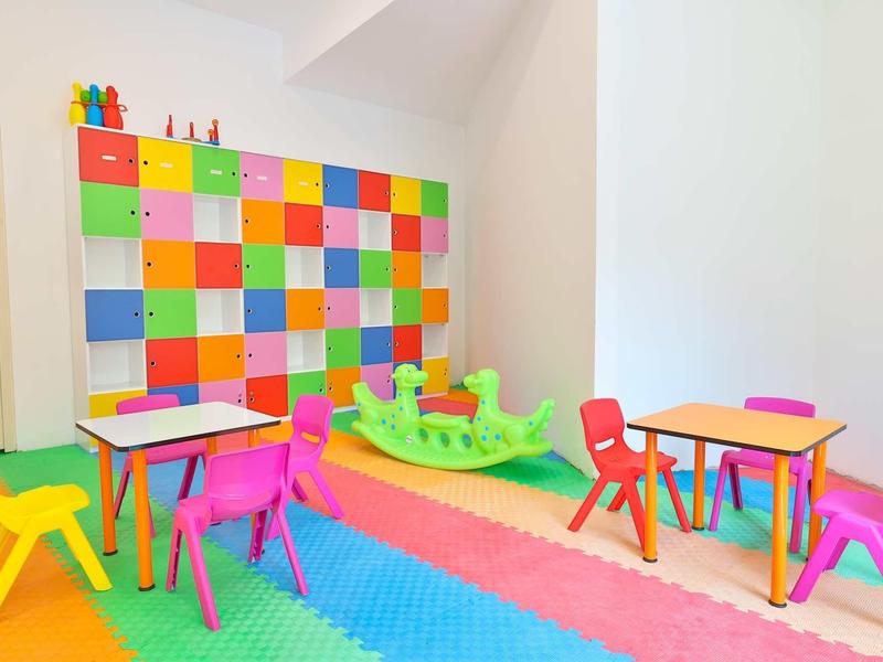Barevná herna pro děti s jasnými židličkami, stoly a lezeckou lodí.