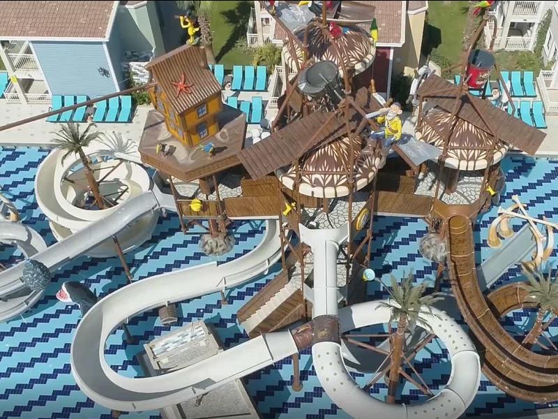 Vodní park s tobogány a rušnou oblastí obklopenou budovami v resortu.