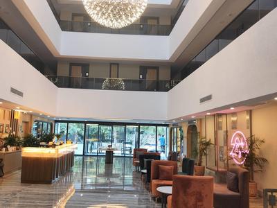 Großer heller Hotellobby mit Sitzgruppen, Bar, Glasfront und Kronleuchter an der Decke.