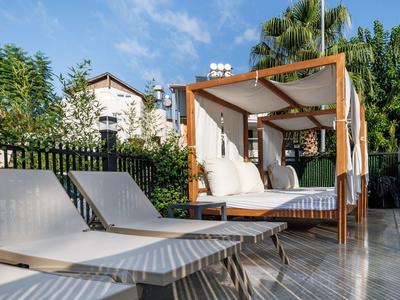 Moderner Außenbereich mit Liegestühlen und einem überdachten Lounge-Bett auf Holzboden bei Sonnenschein.