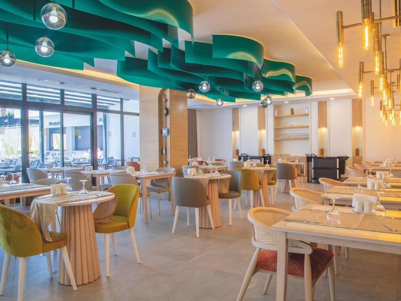 Modern restaurant with colorful chairs, round tables, and decorative ceiling lighting.