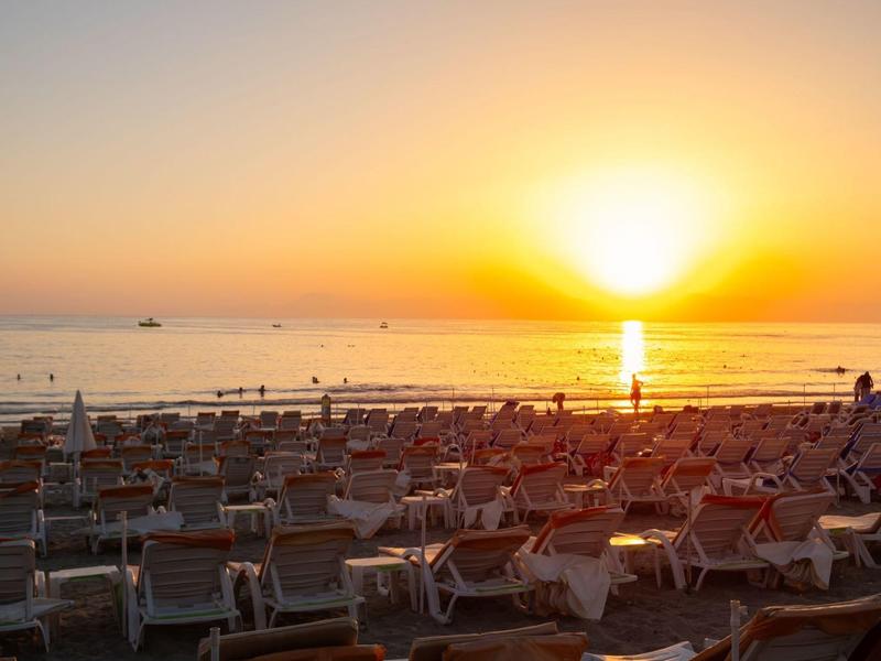 Sunset over beach with many lounge chairs and sailors on the horizon.