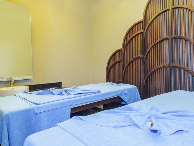 Two massage tables with blue sheets and a privacy screen in the spa room.